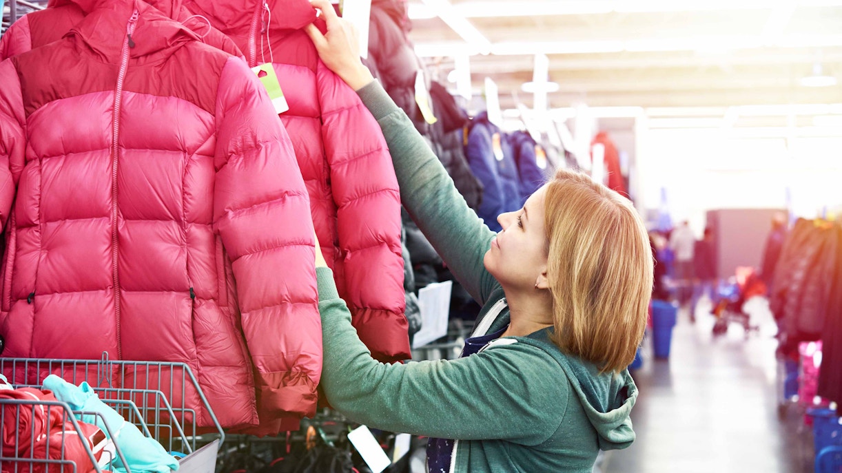 Person browsing red winter jackets in a store aisle.
