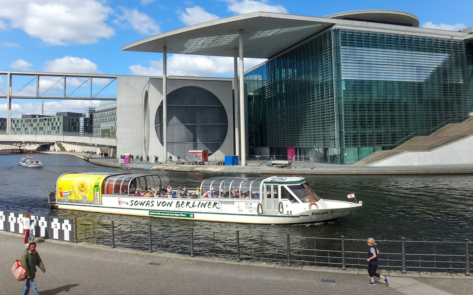 Berlin sightseeing cruise boat on the Spree River near modern government buildings.