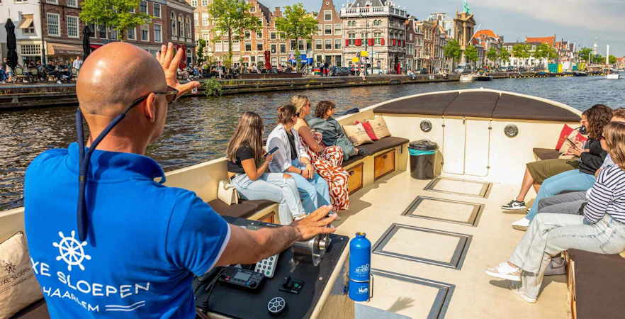 Open boat cruise on Haarlem canal with guide and tourists enjoying city views.