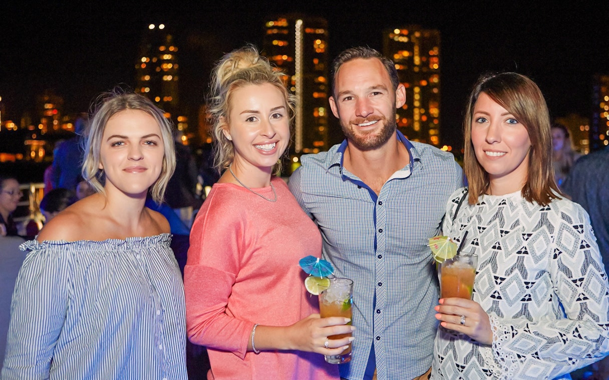 Guests enjoying drinks on a buffet dinner cruise with city skyline in the background.