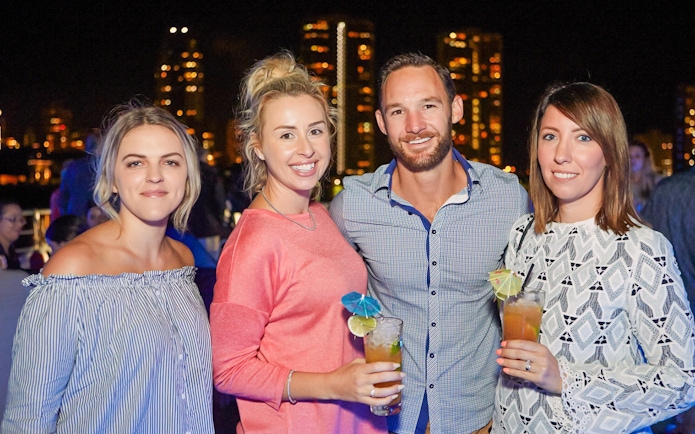 Guests enjoying drinks on a buffet dinner cruise with city skyline in the background.