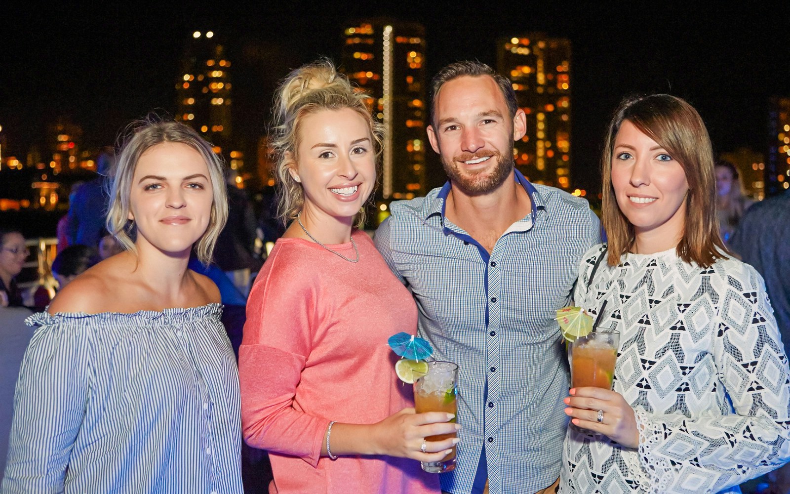 Guests enjoying drinks on a buffet dinner cruise with city skyline in the background.