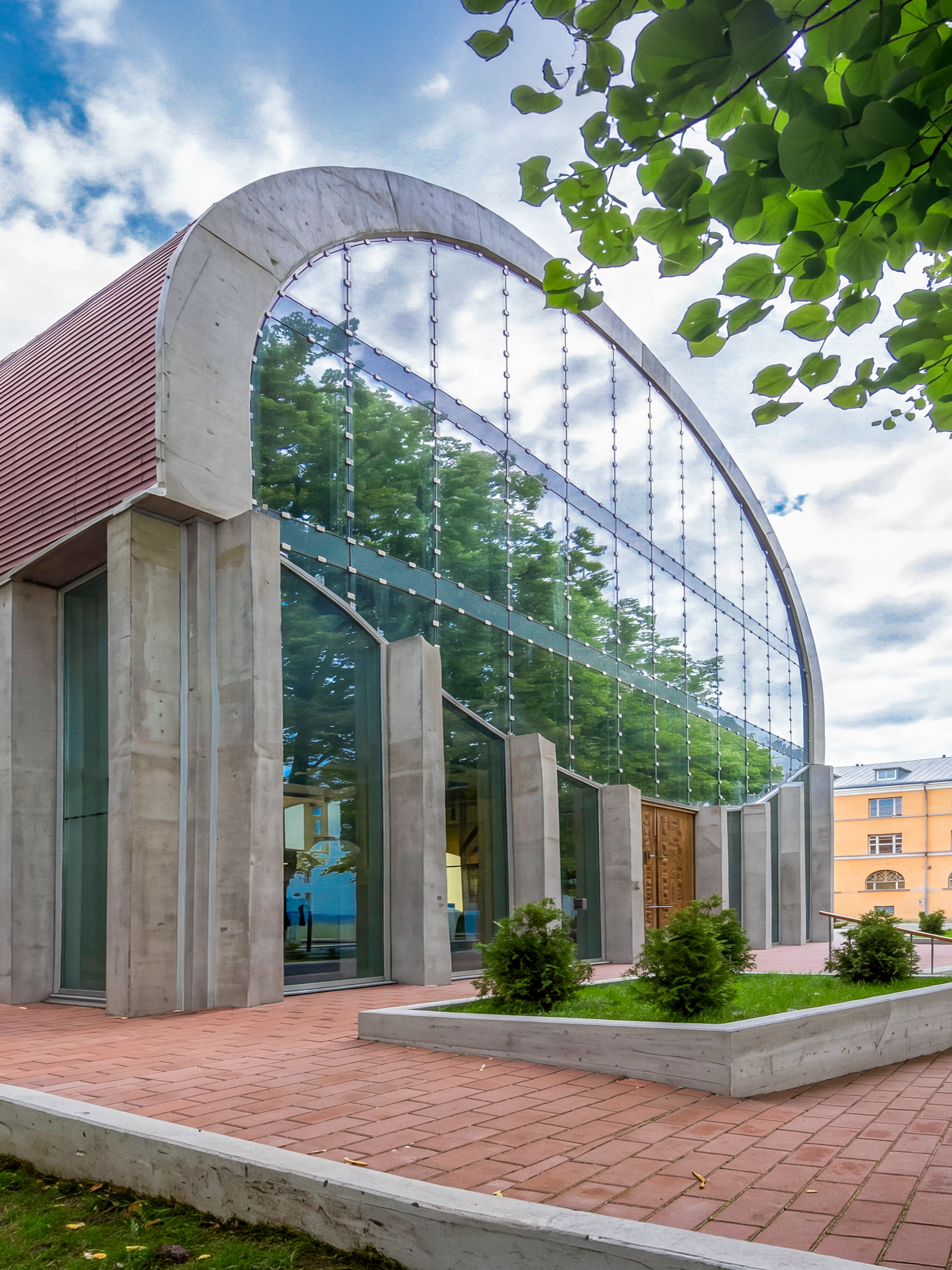 Tallinn Synagogue with modern glass facade and curved roof, surrounded by trees.