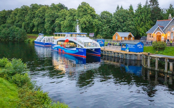 Cruise boat docked at Loch Ness with surrounding greenery, part of the Highlands tour from Edinburgh.