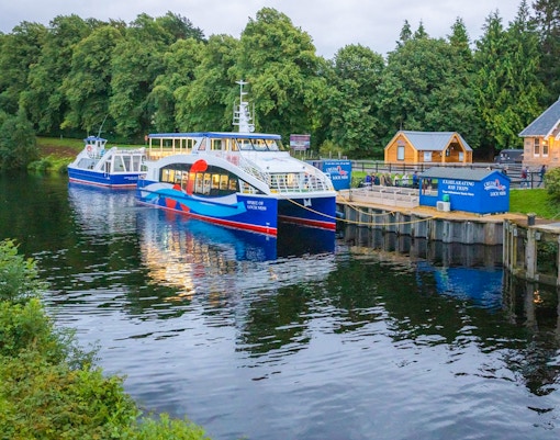 Cruise boat docked at Loch Ness with surrounding greenery, part of the Highlands tour from Edinburgh.