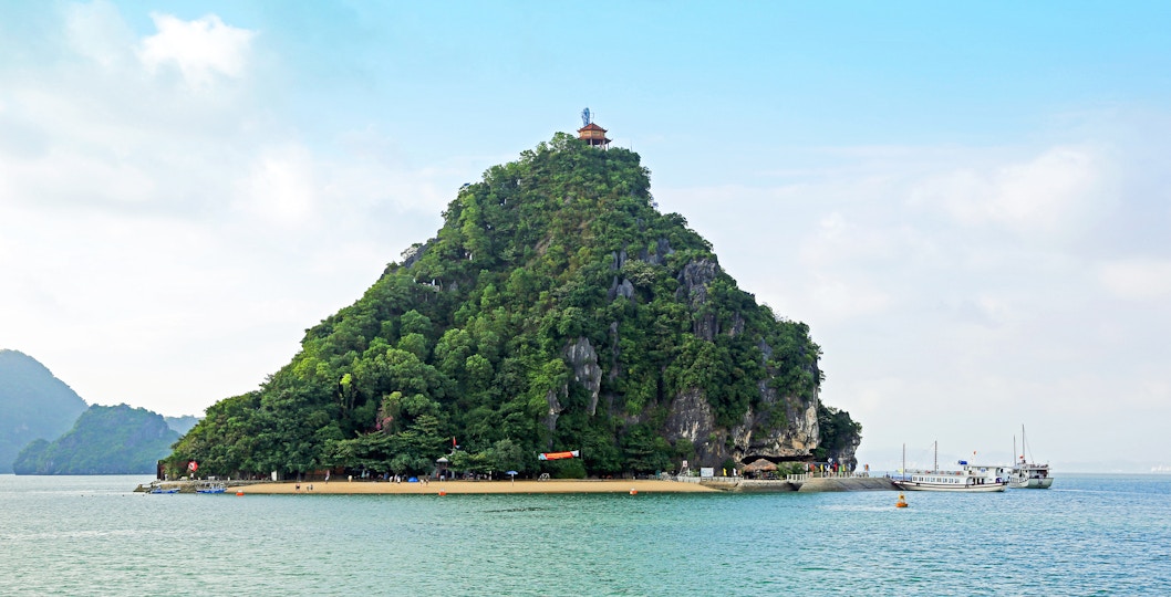 Dao Titop Island in Halong Bay with boats and limestone karsts in the background.