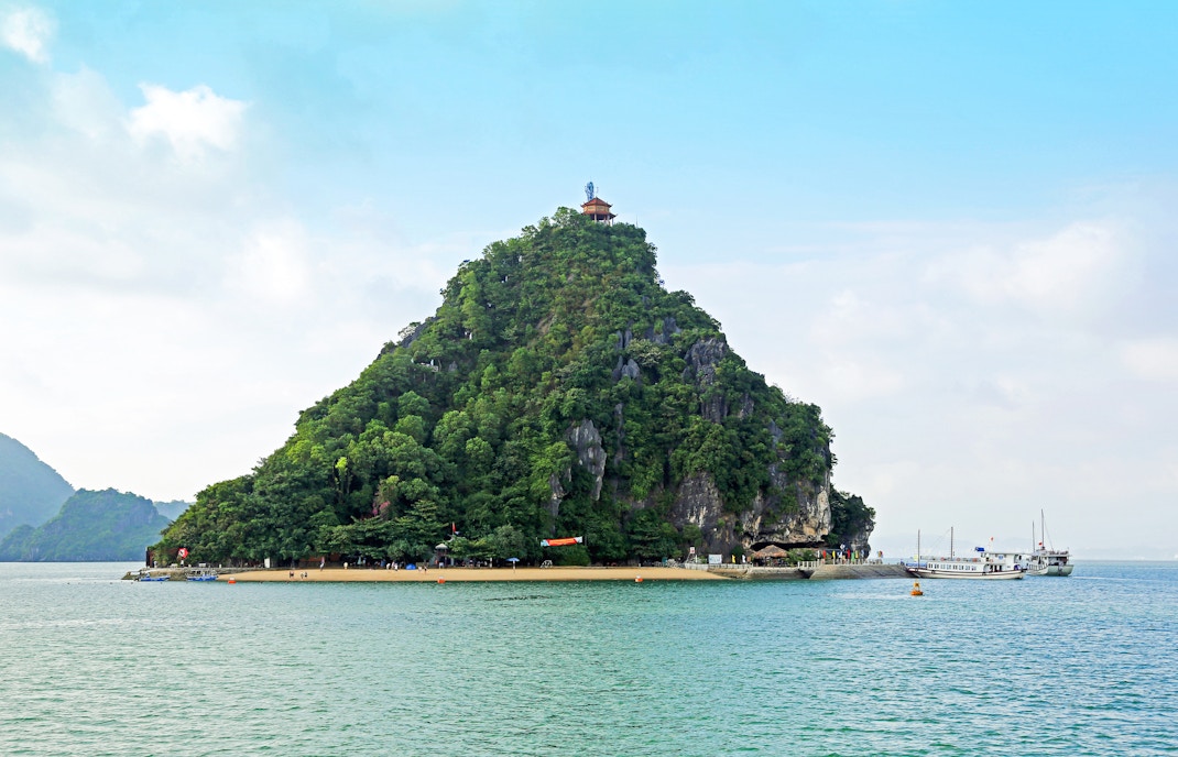 Dao Titop Island in Halong Bay with boats and limestone karsts in the background.
