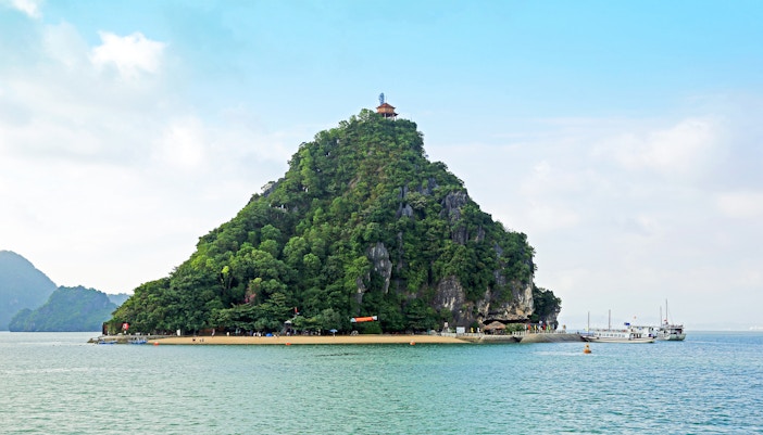 Dao Titop Island in Halong Bay with boats and limestone karsts in the background.