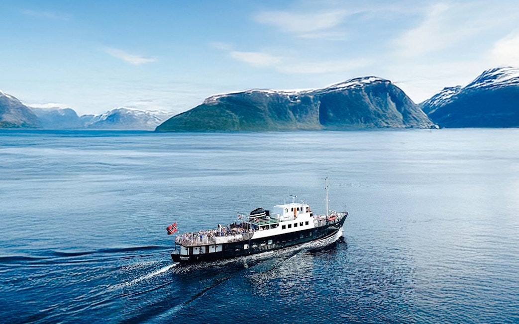 Sightseeing cruise ship on Hjørundfjord, Norway with scenic mountain backdrop.