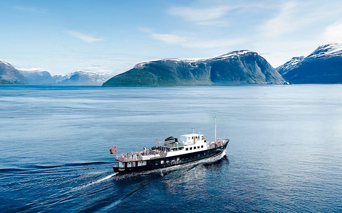 Sightseeing cruise ship on Hjørundfjord, Norway with scenic mountain backdrop.