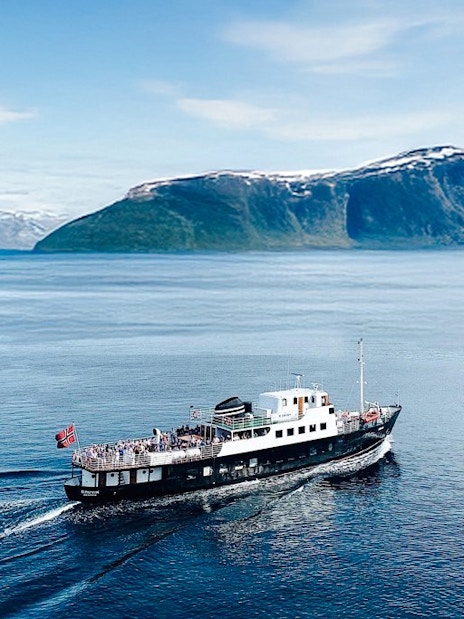 Sightseeing cruise ship on Hjørundfjord, Norway with scenic mountain backdrop.