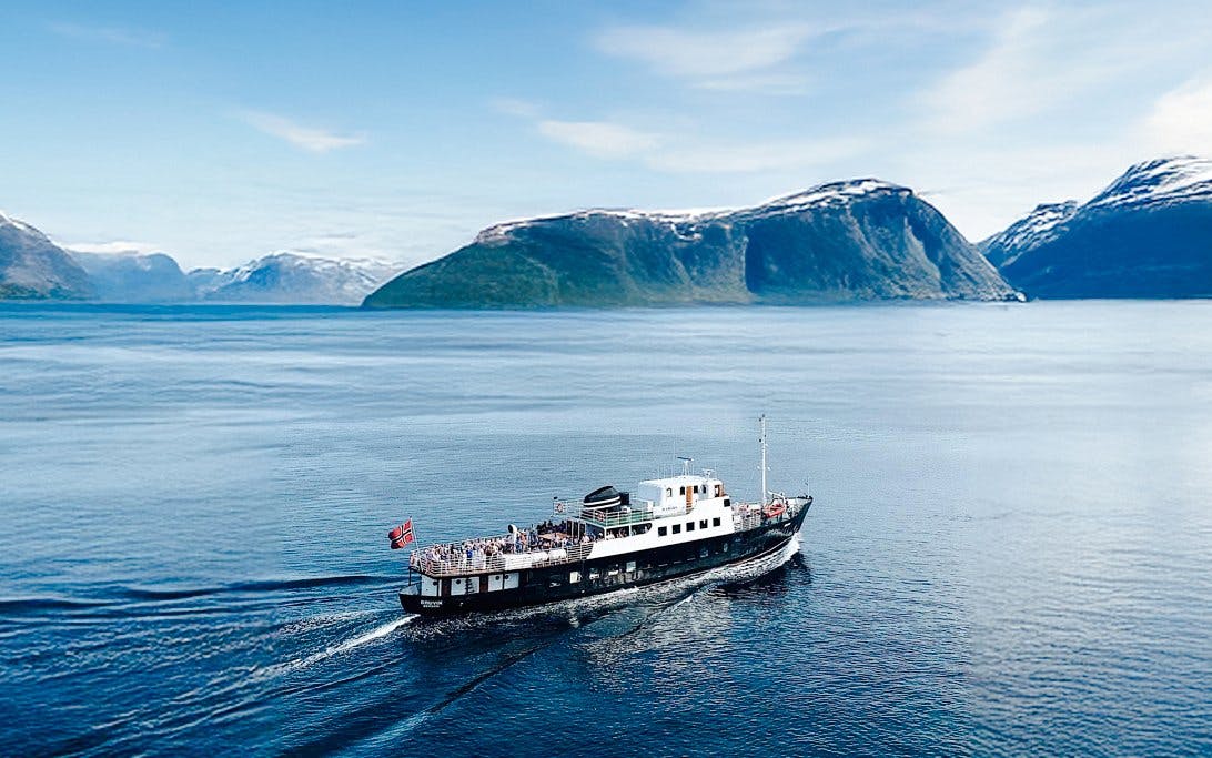 Sightseeing cruise ship on Hjørundfjord, Norway with scenic mountain backdrop.
