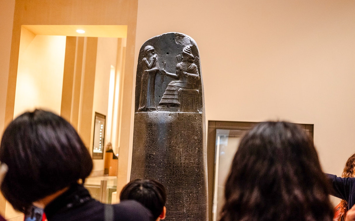 Tourists viewing the Code of Hammurabi with a guide inside the Louvre Museum, France.