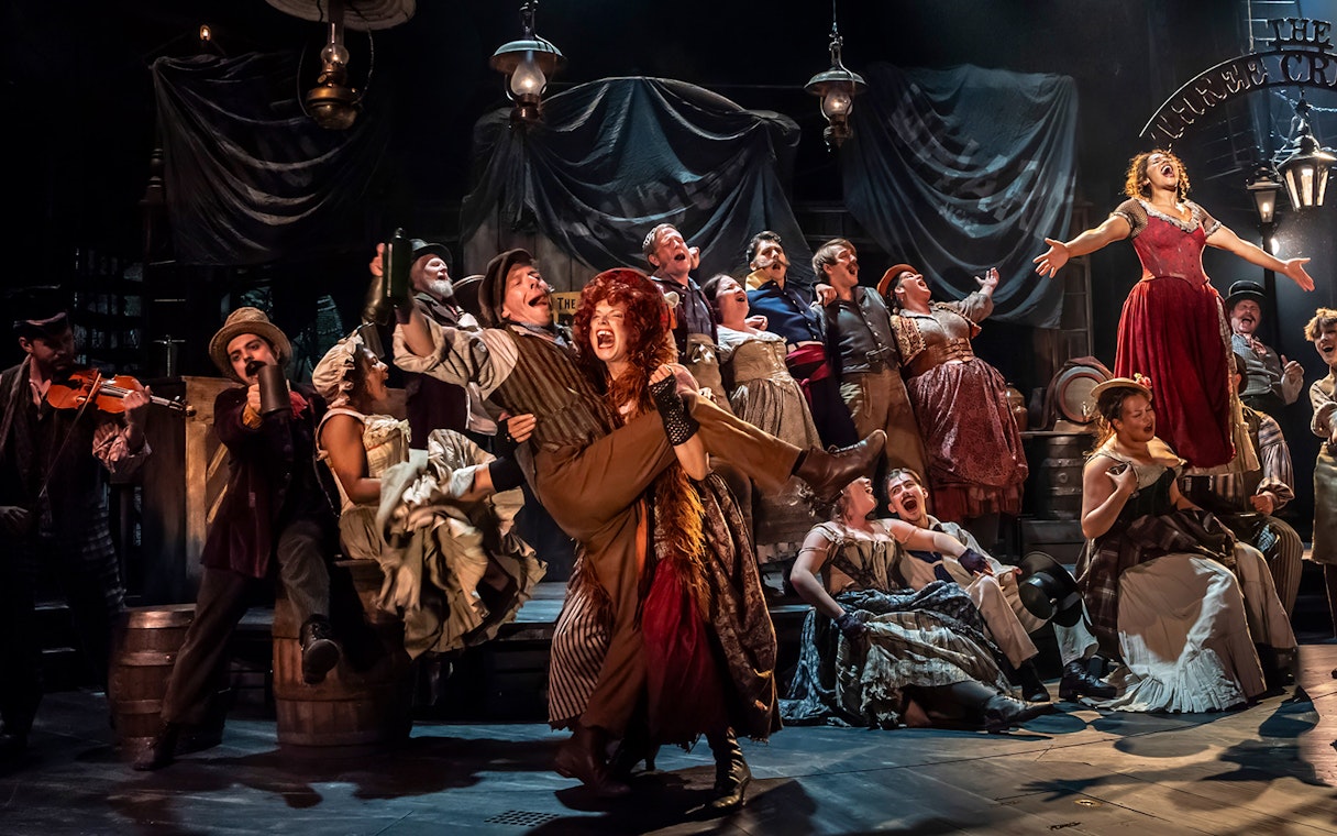 Cast performing a lively scene from the musical Oliver! on stage with vibrant costumes.