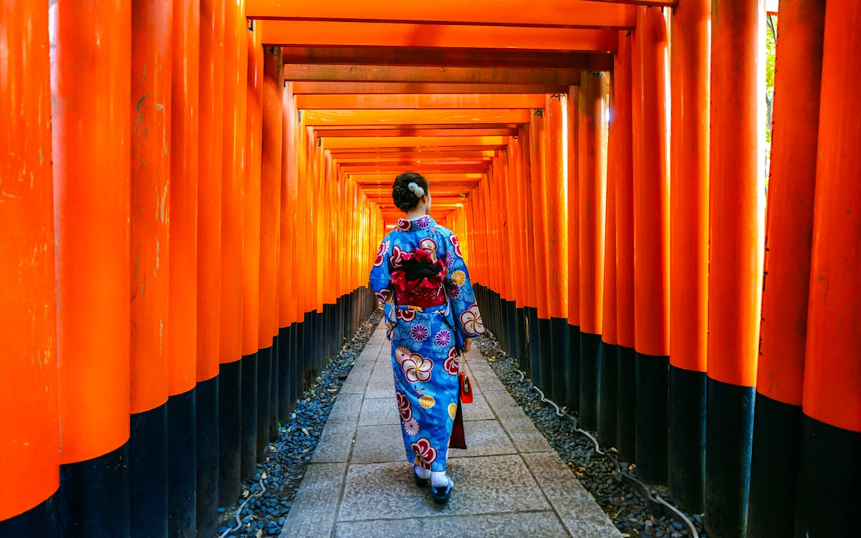 Person in kimono walking through orange torii gates at Fushimi Inari Taisha, Kyoto.