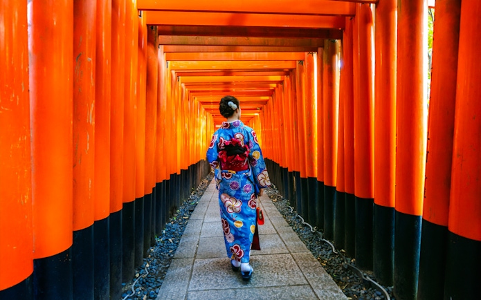 Person in kimono walking through orange torii gates at Fushimi Inari Taisha, Kyoto.