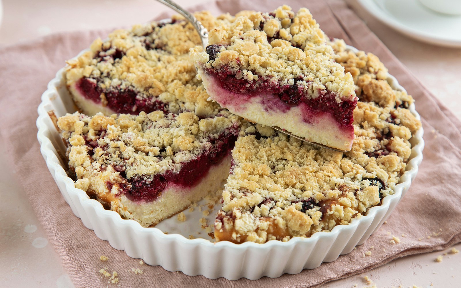 Ricotta and sour cherry tart with crumbly topping in a white dish.