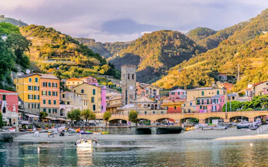 Colorful buildings and clock tower in Monterosso al Mare, Italy, with hills in the background.