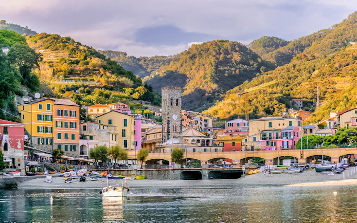 Colorful buildings and clock tower in Monterosso al Mare, Italy, with hills in the background.