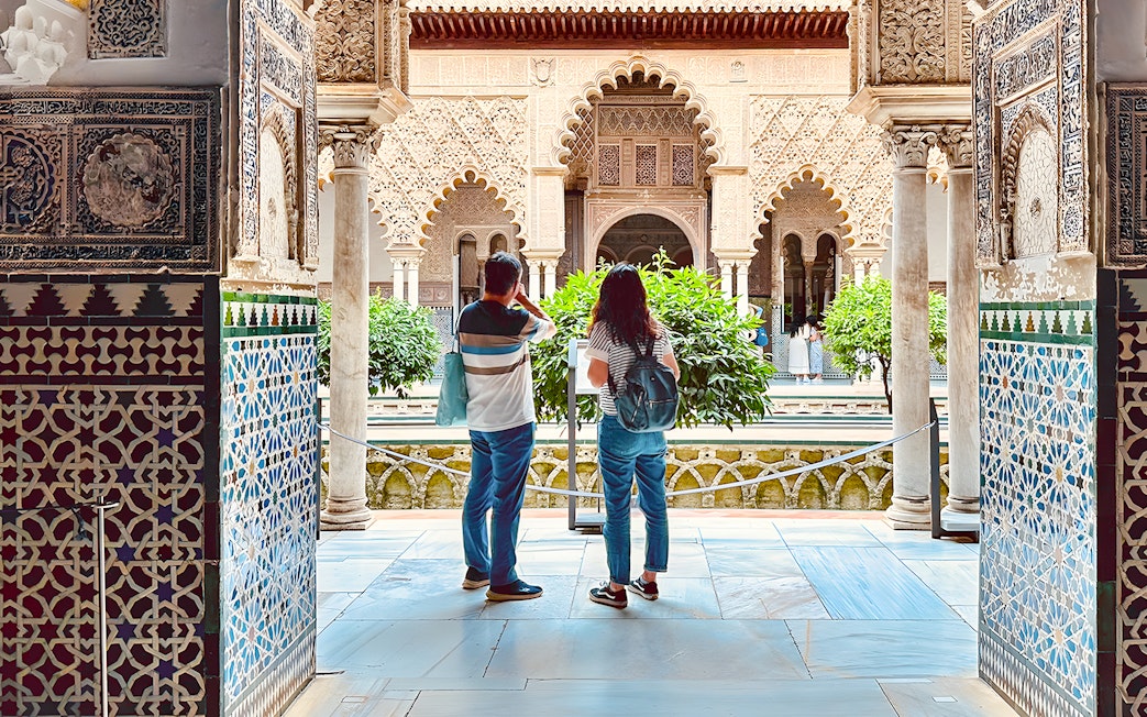 Tourists listening to guide in Royal Alcazar of Seville courtyard, Seville, Spain.