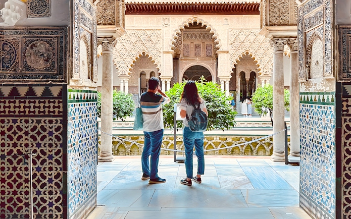 Tourists listening to guide in Royal Alcazar of Seville courtyard, Seville, Spain.