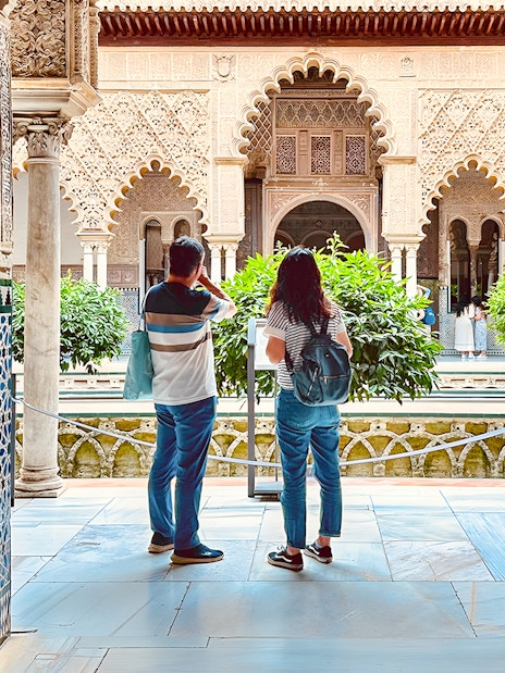 Tourists listening to guide in Royal Alcazar of Seville courtyard, Seville, Spain.
