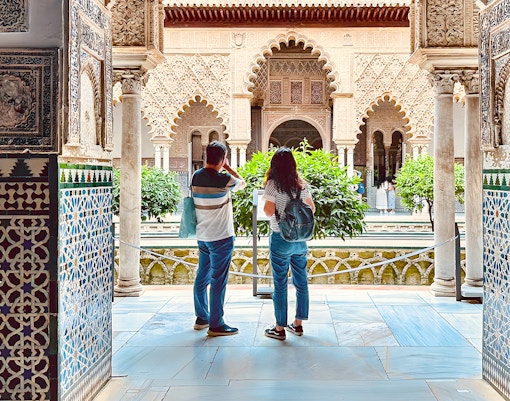 Tour guide explaining Royal Alcazar of Seville courtyard history to Asian-language tour group in Seville, Spain.