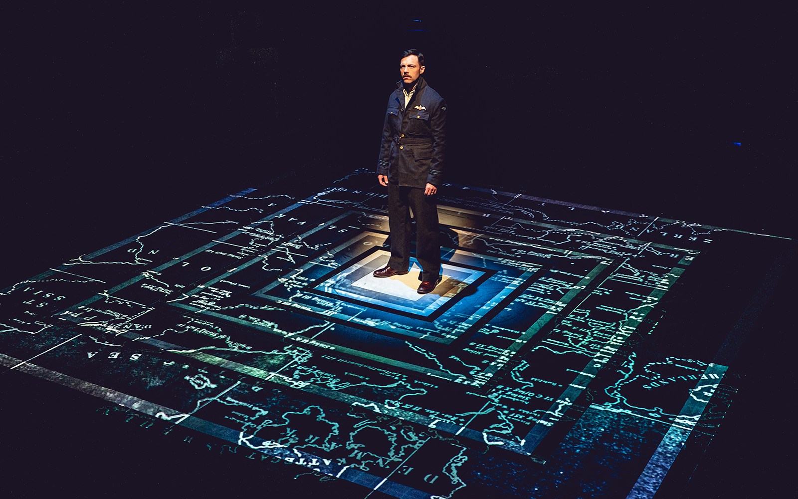 Man in uniform standing on a projected map, related to Tom, Dick and Harry tour.