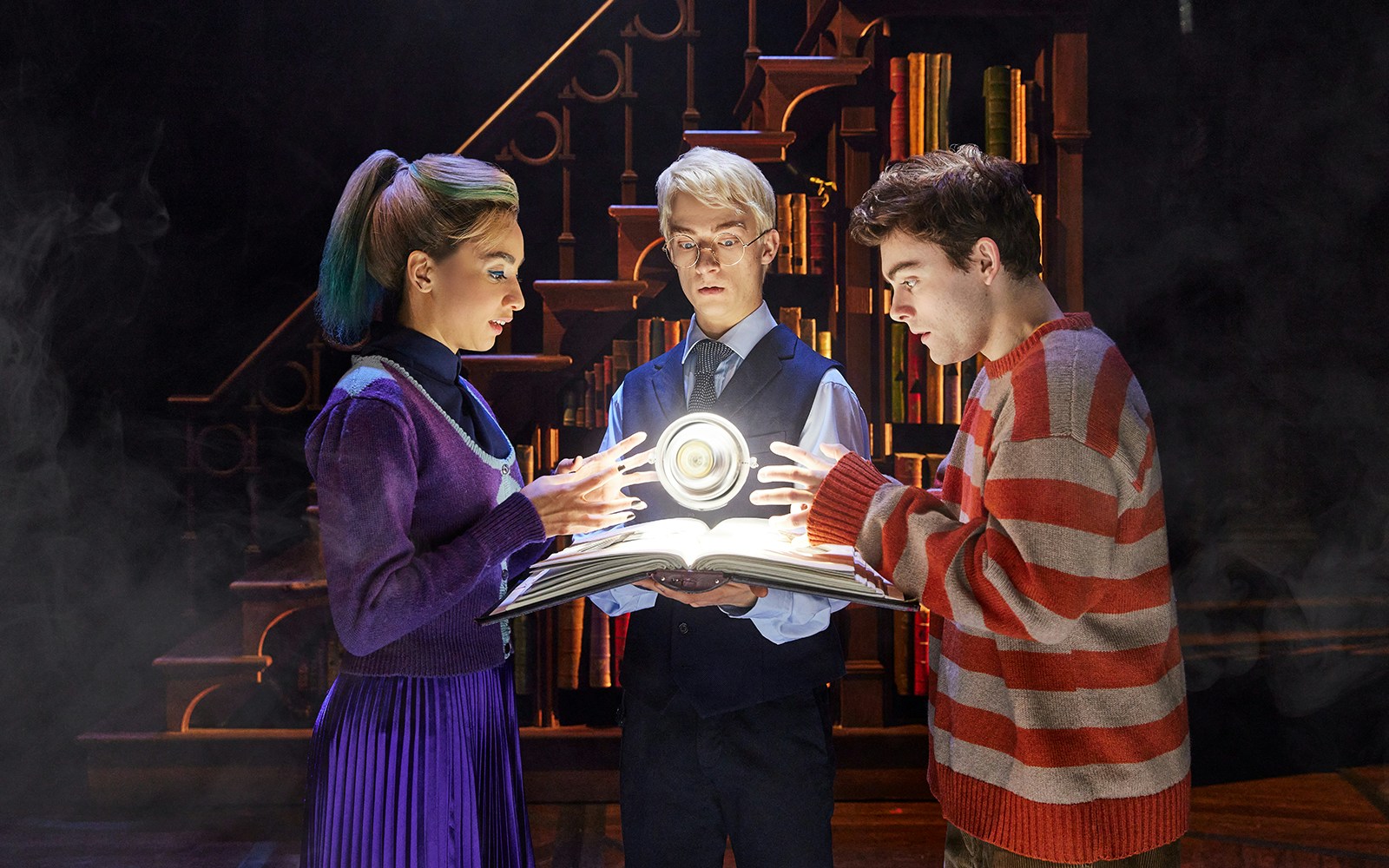 Characters examining a glowing book in "Harry Potter and the Cursed Child" stage scene.