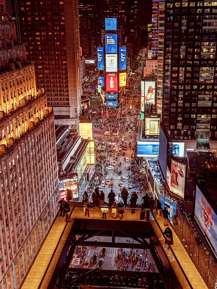Visitors on One Times Square Skywalk overlooking bustling Times Square at night, New York City.