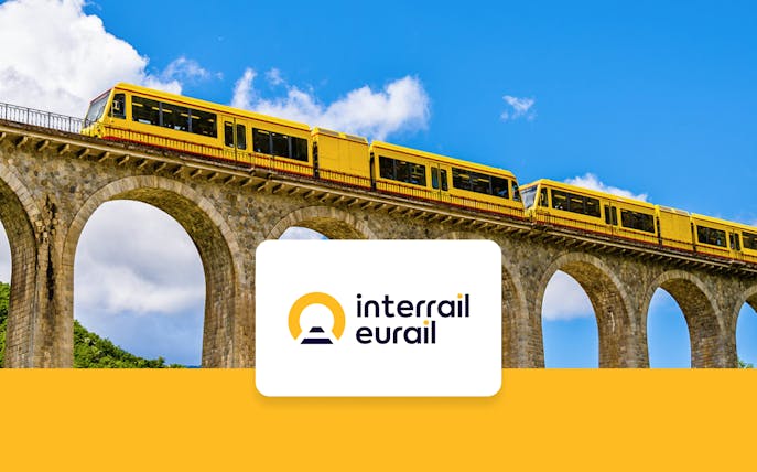 Yellow train crossing a stone viaduct under a blue sky, promoting Interrail Global Mobile Pass Flex.