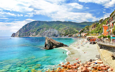 Monterosso al Mare coastline with beachgoers and colorful buildings, Italy.