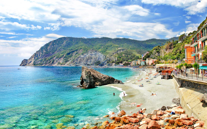 Monterosso al Mare coastline with beachgoers and colorful buildings, Italy.