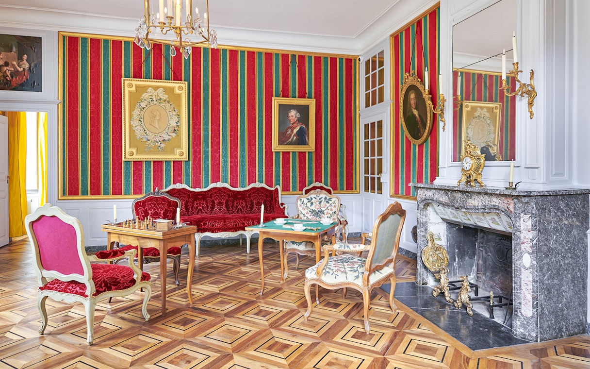 Elegant room in Voltaire's castle with ornate furniture and decorative fireplace.