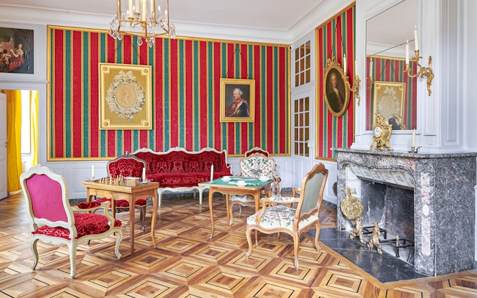 Elegant room in Voltaire's castle with ornate furniture and decorative fireplace.