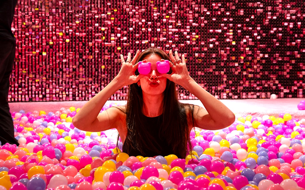 Visitor in Gummy Bear Pool at Museum of Candy, Dubai holding pink bears over eyes.