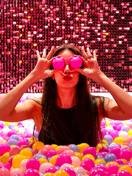 Visitor in Gummy Bear Pool at Museum of Candy, Dubai holding pink bears over eyes.