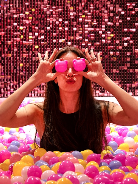 Visitor in Gummy Bear Pool at Museum of Candy, Dubai holding pink bears over eyes.