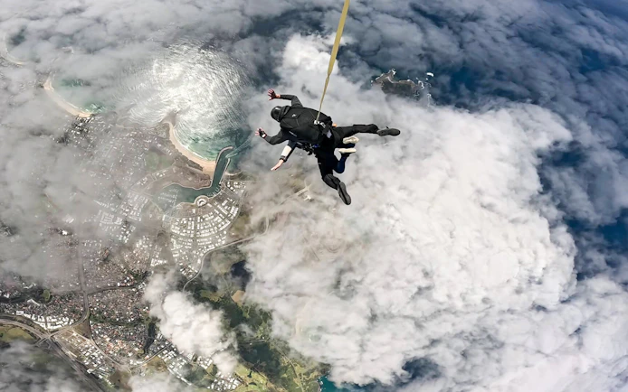 Skydivers descending over Shellharbour, Sydney, with coastal view from 15,000 feet.