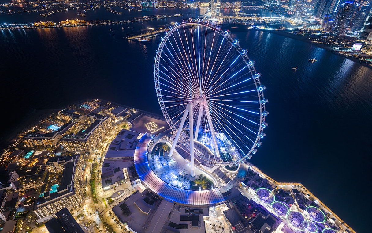 Aerial view of Ain Dubai illuminated at night with cityscape in the background.