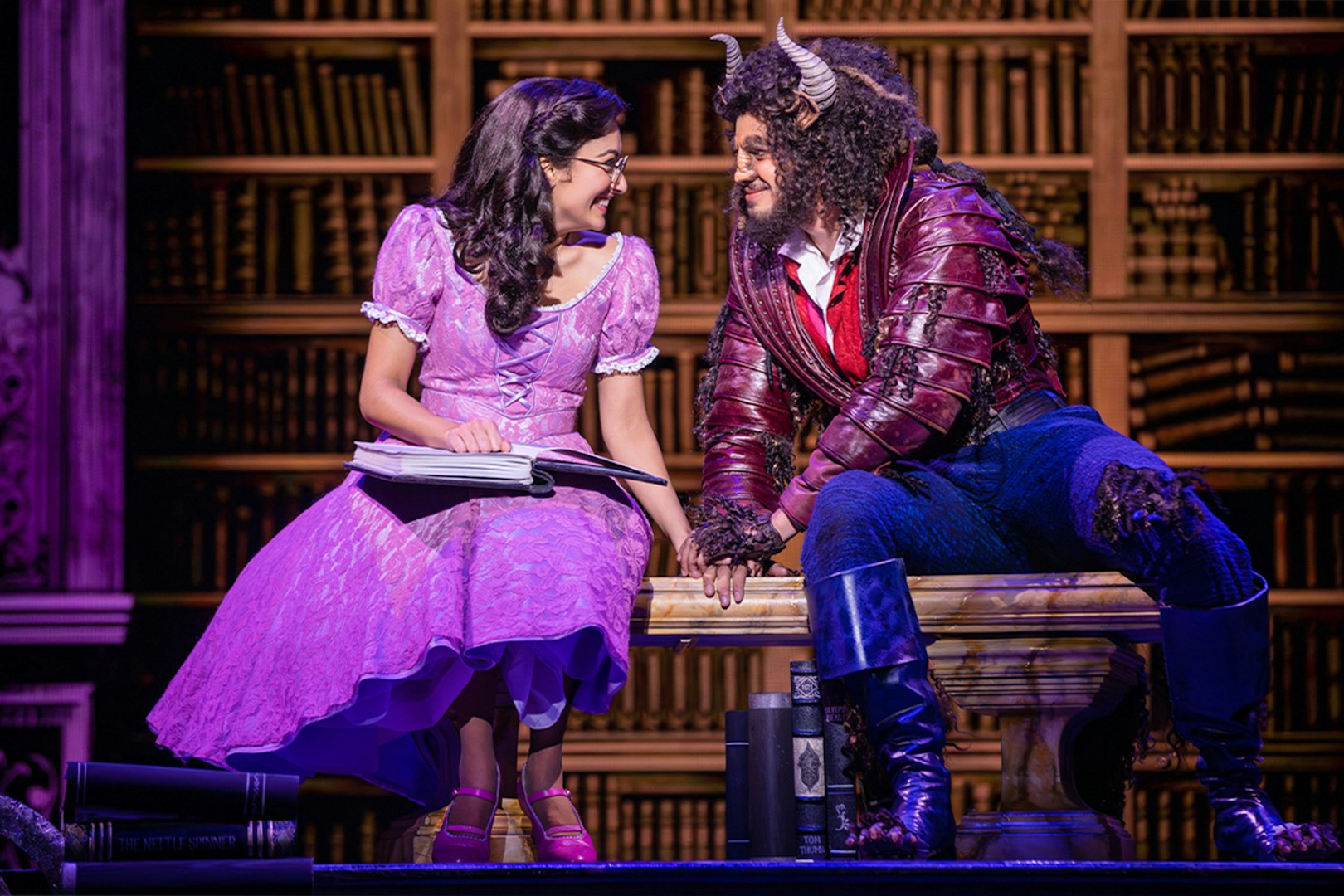 Belle and Beast sharing a moment in a library setting during a Beauty and the Beast performance.