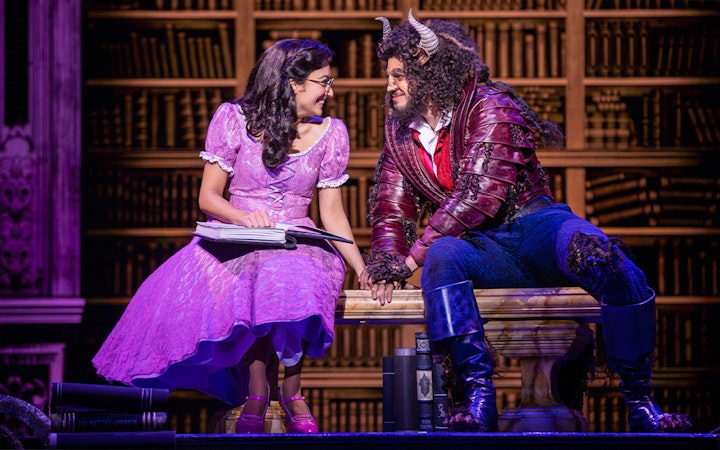 Belle and Beast sharing a moment in a library setting during a Beauty and the Beast performance.