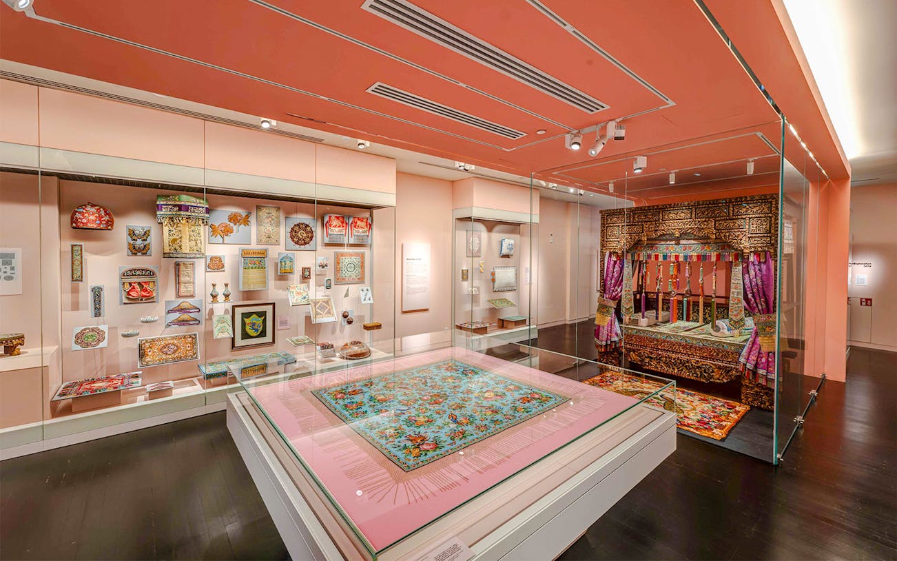 Peranakan Museum gallery with traditional textiles and ornate wooden bed display.