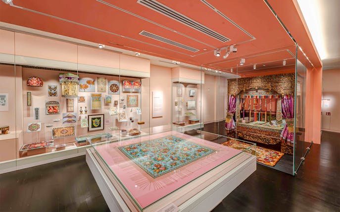 Peranakan Museum gallery with traditional textiles and ornate wooden bed display.