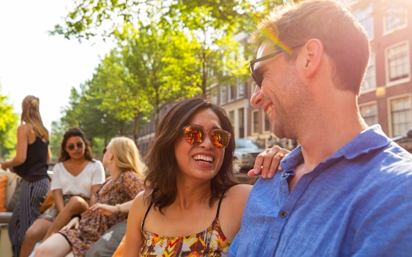 Couple enjoying a canal cruise in Amsterdam with friends, surrounded by historic buildings.