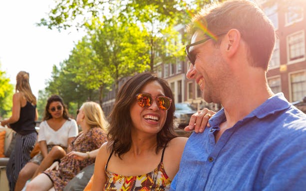 Couple enjoying a canal cruise in Amsterdam with friends, surrounded by historic buildings.