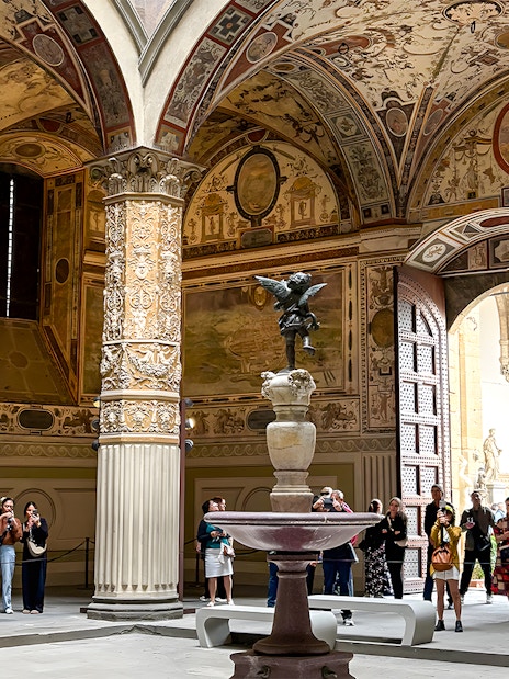 Tourists exploring the ornate courtyard of Palazzo Vecchio in Florence.