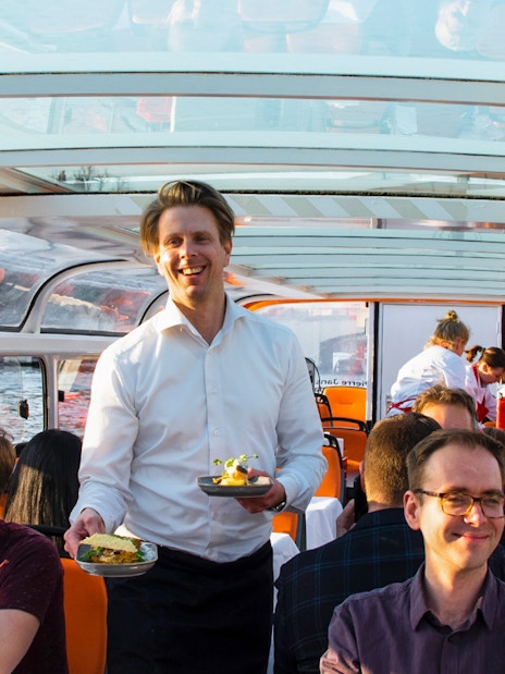 Service staff serving meals on a dinner cruise boat with guests dining.
