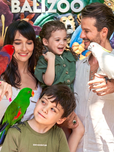 Family with colorful parrots in front of a mural at Bali Zoo.