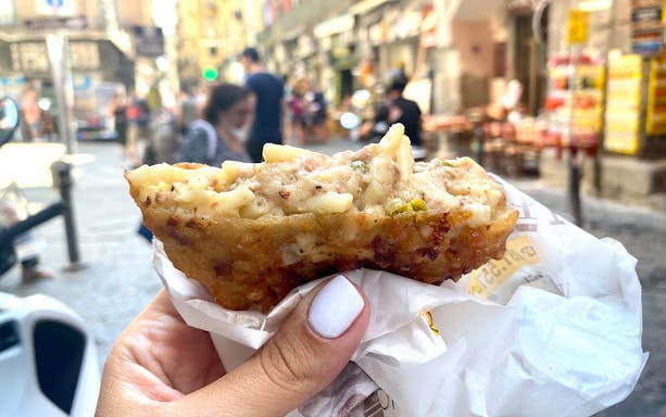 Hand holding a fried pasta street food in Naples, Italy.